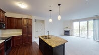 This single-floor residence offers a thoughtfully designed open-concept layout that seamlessly connects the kitchen and living areas. The kitchen is a standout feature, equipped with rich, dark cherry wood cabinetry offering generous storage, stainless steel appliances including a French door refrigerator, electric range, and built-in microwave. A central island with a granite countertop and undermount sink serves as a functional focal point, illuminated by stylish pendant lighting overhead. Hardwood flooring anchors the kitchen and transitions into plush wall-to-wall carpeting throughout the living areas and bedrooms. The spacious living room is highlighted by a tiled fireplace and sliding glass doors that open to a private balcony, allowing abundant natural light and outdoor views. The bedrooms are well-sized with large windows that bring in natural light. The bathroom is cleanly finished with tile flooring, a full tub-shower combination, and a dark-cabineted vanity with a white countertop. A dedicated in-unit laundry area with full-size washer and dryer hookups, overhead cabinetry, and a wire shelving rack adds everyday convenience. The overall ambiance is warm, functional, and move-in ready.