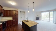 This single-floor residence offers a thoughtfully designed open-concept layout that seamlessly connects the kitchen and living areas. The kitchen is a standout feature, equipped with rich, dark cherry wood cabinetry offering generous storage, stainless steel appliances including a French door refrigerator, electric range, and built-in microwave. A central island with a granite countertop and undermount sink serves as a functional focal point, illuminated by stylish pendant lighting overhead. Hardwood flooring anchors the kitchen and transitions into plush wall-to-wall carpeting throughout the living areas and bedrooms. The spacious living room is highlighted by a tiled fireplace and sliding glass doors that open to a private balcony, allowing abundant natural light and outdoor views. The bedrooms are well-sized with large windows that bring in natural light. The bathroom is cleanly finished with tile flooring, a full tub-shower combination, and a dark-cabineted vanity with a white countertop. A dedicated in-unit laundry area with full-size washer and dryer hookups, overhead cabinetry, and a wire shelving rack adds everyday convenience. The overall ambiance is warm, functional, and move-in ready.