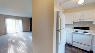 Located at 601 Wenger Rd. in Englewood, Ohio, this single-floor unit offers a well-organized and functional layout throughout. The living room is a standout space, featuring a striking full-height exposed brick accent wall that adds character and warmth, plush carpeted flooring, and a large sliding glass door with vertical blinds that floods the room with natural light and provides outdoor access. A thermostat and cable connections are conveniently positioned on the adjacent wall. The kitchen is efficiently designed with white cabinetry, white appliances including a refrigerator, electric range, and a stainless steel sink, complemented by wood-look vinyl flooring and a window that brings in additional natural light. The bedrooms are carpeted and bathed in natural light from windows with blinds; one bedroom features a double closet offering generous storage. The unit includes two bathrooms, each with wood-look vinyl flooring, white vanities with mirrored medicine cabinets or lighted mirrors, and clean, functional finishes. Warm neutral tones are carried throughout the unit, creating a cohesive and inviting atmosphere from room to room.