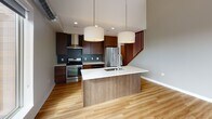 Located in Minneapolis's dynamic Uptown neighborhood, this two-story residence offers a thoughtfully designed layout across two well-appointed levels. The main floor showcases an open-concept living area with light hardwood flooring and soaring ceilings, creating a bright and airy atmosphere. Exposed industrial-style ductwork adds an urban character to the space, while large floor-to-ceiling windows frame expansive views of the Minneapolis skyline.

The kitchen is a standout feature, equipped with rich dark-wood cabinetry, stainless steel appliances including a gas range and French door refrigerator, a striking teal tile backsplash, and a large center island with a white quartz countertop and integrated sink. Pendant lighting and recessed fixtures complete the polished look. A stylishly appointed bathroom on this level features dark large-format tile flooring and warm wood vanity cabinetry.

A distinctive wood-slatted staircase leads to the upper level, where an open loft-style landing overlooks the main floor. The upper level hosts generously sized bedrooms with plush carpeting, ample closet space, and large windows that fill each room with natural light. The upper-level full bathroom features a glass-enclosed walk-in shower with teal tile surround, a dual-sink vanity, and dark tile flooring, reflecting the same contemporary design sensibility found throughout this well-crafted home.