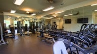 Located at 10210 Hillston Ridge Rd in Raleigh, NC, this single-floor fitness center offers a well-equipped workout environment designed to support a variety of exercise routines. The space is outfitted with professional-grade equipment, including Cybex cardio machines, a full dumbbell rack with an extensive range of free weights, and multiple cable and strength training machines. Floor-to-ceiling mirrors line the walls, creating an open, expansive feel while allowing users to monitor their form during workouts. The durable rubber flooring provides cushioning and stability throughout the space. Overhead fluorescent lighting ensures the room is bright and well-illuminated, and ceiling fans help maintain air circulation during intense workouts. A wall-mounted flat-screen television adds an entertainment option for those looking to stay engaged during cardio sessions. The layout is thoughtfully organized, providing ample room to move between equipment stations comfortably. Overall, the fitness center presents a clean, functional, and professional atmosphere suited for both focused strength training and general fitness activities.