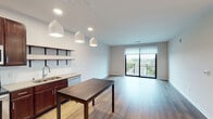 This well-appointed single-floor unit offers a thoughtfully designed open-concept layout that seamlessly connects the kitchen, dining, and living areas. The kitchen is a standout feature, showcasing rich dark-wood cabinetry, stainless steel appliances including a refrigerator, electric range, and built-in microwave, along with a double-basin sink, light quartz-style countertops, a subway tile backsplash, and open wall-mounted shelving. Pendant lighting above the dining area adds a contemporary touch, while light hardwood-style flooring runs throughout the main living space. The living area extends toward a large sliding glass door that opens to a private balcony, allowing ample natural light and outdoor views of surrounding greenery. The two bedrooms are finished with plush neutral carpeting and feature large windows that frame views of the landscaped surroundings. One bedroom includes a spacious walk-in closet with dual wire shelving systems. The unit includes two bathrooms, each finished with dark wood vanities, light countertops, and hardwood-style flooring. One bathroom offers a full walk-in shower, while the other provides a streamlined vanity and toilet configuration. The overall aesthetic is clean, modern, and functional throughout.