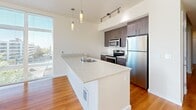 Located in Seattle's Capitol Hill neighborhood, this thoughtfully designed one-bedroom, one-bathroom residence offers a clean, modern aesthetic across a single floor. Warm hardwood flooring flows throughout the living areas, complementing the crisp white walls and creating a welcoming atmosphere.

The open-concept kitchen and living area serves as the heart of the home. The kitchen is outfitted with stainless steel appliances — including a range, microwave, and full-size refrigerator — paired with warm wood cabinetry and stone-finish countertops. A peninsula with an undermount sink provides additional prep space and serves as a natural divider between the kitchen and living area. Pendant lighting and track lighting add functional style overhead.

The living room is bathed in natural light thanks to expansive floor-to-ceiling windows that frame sweeping views of the Seattle skyline and surrounding cityscape, extending the sense of space well beyond the interior.

The bedroom is a quiet, well-proportioned retreat, also benefiting from large windows with city views and hardwood flooring. Two closets provide ample storage.

The bathroom features a wood-toned vanity with stone-finish countertops, an undermount sink, and large mirrors that reflect light throughout the space. Sliding doors and recessed lighting add to the unit's clean, contemporary finish.