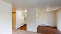 This single-floor residence offers a practical, open-concept layout connecting the main living areas in a cohesive and functional arrangement. The living and dining area features warm hardwood-style flooring and transitions seamlessly to carpeted zones, providing a comfortable contrast underfoot. A baseboard heating unit runs along the wall, and a sliding glass door with vertical blinds and an adjacent window allow natural light to fill the space while offering outdoor views of surrounding greenery.

The kitchen is defined by a wraparound peninsula layout with light-toned countertops and a built-in single-basin sink. White cabinetry with warm wood-tone trim provides generous storage along the upper and lower walls, while white appliances—including a refrigerator, electric range, and dishwasher—complete the functional setup. Fluorescent overhead lighting ensures the kitchen remains well-lit.

The bedroom is carpeted and features a ceiling fan, a window with natural views, and a mirrored sliding closet with built-in shelving for organized storage. The bathroom includes a wide vanity with a large mirror, an overhead light, and a tub-shower combination. A washer and dryer unit is also visible, indicating in-unit laundry convenience. Textured ceilings are consistent throughout the space.