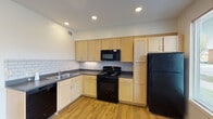 Located at 1011 W Jefferson St in Louisville, Kentucky, this single-story unit offers a well-designed layout with consistent wood-look flooring throughout. The kitchen is a functional centerpiece, featuring light wood cabinetry paired with white lower cabinets, dark countertops, and a classic white subway tile backsplash. Black appliances — including a gas range, over-the-range microwave, dishwasher, and refrigerator — complete the kitchen, which is illuminated by recessed lighting overhead.

The open living area flows naturally from the kitchen and is brightened by a ceiling fan with light fixture and access to an exterior door, providing a connection to the outdoors. Multiple windows allow natural light to fill the rooms, particularly in a well-lit bedroom area featuring corner windows that offer views of the surrounding neighborhood and contribute to an airy feel.

The bathroom is clean and practical, with a warm wood vanity, white countertop, large mirror, and wood-look flooring that carries through from the rest of the unit. The overall layout, visible in the 3D overview, is efficiently organized and offers comfortable, move-in-ready living in a convenient Louisville location.