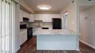 Located at 20800 Riverterrace Rd in South Chesterfield, Virginia, this single-story residence is designed with a clean, modern aesthetic throughout. Dark hardwood-style flooring runs continuously across the living areas, bedrooms, and kitchen, providing a cohesive and polished look.

The open living area is bright and spacious, featuring a sliding glass door dressed with vertical blinds that allows natural light to pour in and provides views of the surrounding greenery. The space flows directly into the kitchen, which is separated by a peninsula-style island topped with granite countertops featuring subtle veining. The kitchen is well-appointed with crisp white shaker cabinetry, matching granite countertops along the perimeter, black appliances including a range, refrigerator, and dishwasher, and a stainless steel sink.

The bedrooms are generously sized with neutral gray walls and large windows that invite natural light. Each bedroom offers notable closet space, with some rooms featuring dual closets fitted with hanging rods. One bedroom includes convenient access to a private bathroom. Throughout the residence, the neutral color palette, clean lines, and consistent flooring create a calm, move-in-ready atmosphere.