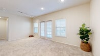 This single-floor space offers a thoughtfully designed layout with a neutral, light-filled aesthetic throughout. The main living area is generously sized, featuring soft wall-to-wall carpeting in a warm beige tone and multiple windows dressed with white horizontal blinds that allow natural light to filter in comfortably. A set of French doors provides direct outdoor access, enhancing the sense of openness. Track lighting runs along one side of the ceiling, complementing the recessed can lights overhead and offering flexible illumination options.

The kitchen is well-equipped and features shaker-style cabinetry in a soft grey-white finish, paired with speckled granite countertops and a classic white subway tile backsplash. Stainless steel appliances, including a side-by-side refrigerator and range, provide a modern, functional workspace. Wood-look flooring grounds the kitchen with a warm contrast to the cabinetry.

A secondary carpeted room offers a ceiling fan and a window with outdoor views, making it a versatile space suitable as a bedroom or office. The bathroom includes a walk-in shower enclosed by a frameless glass door, finished with white subway tile walls, a built-in niche, and chrome hardware for a clean, contemporary look.