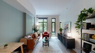 This well-designed one-bedroom, one-bathroom unit offers a thoughtfully organized layout across a single floor, making efficient use of every square foot. The living room serves as the centerpiece of the space, featuring large black-framed windows that frame lush greenery outside and fill the room with natural light. A sage green accent wall adds a calming, contemporary touch, complementing the light hardwood flooring that runs throughout.

The galley-style kitchen is outfitted with dark wood cabinetry extending to the ceiling, quartz countertops, a stainless steel appliance suite including a range, dishwasher, and built-in microwave, and a single-basin sink. The kitchen opens directly toward the living area, creating a connected, functional flow.

The bedroom accommodates a full sleeping and workspace setup, with large windows offering tree-lined views, a sliding glass-panel closet door, and warm accent walls that provide a restful atmosphere. A dedicated closet provides additional storage.

The bathroom features a glass-enclosed walk-in shower with dark tile surround, a wood-toned vanity with quartz countertop, an undermount sink, and a backlit oval mirror, delivering a clean, spa-like aesthetic that complements the unit's modern design throughout.
