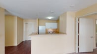 This single-floor unit is designed with a practical, open layout that connects the main living areas seamlessly. The kitchen is positioned near the entryway and features white cabinetry, a white refrigerator, and an electric range. A peninsula counter extends outward, creating a natural boundary between the kitchen and the adjoining living space while offering additional prep or casual dining space. The entryway door opens directly into this area, where rich dark hardwood-style flooring runs throughout the kitchen and hallway zones.

The bedrooms are carpeted and share a consistent warm beige color palette. Each room is equipped with a ceiling fan with integrated lighting and features a window fitted with blinds, allowing for controlled natural light. The rooms offer comfortable proportions suitable for standard bedroom furnishings.

Two bathrooms serve the unit. One features a tub-shower combination, vanity with under-sink cabinetry, a large mirror, and hardwood-style flooring. The second bathroom includes accessibility-focused grab bars alongside the toilet and near the vanity, a wall-mounted mirror with overhead lighting, and the same dark flooring. Both bathrooms maintain the unit's neutral color scheme. Textured ceilings are consistent throughout the space.