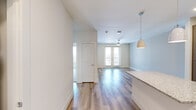 This thoughtfully designed 1-bedroom, 1-bathroom residence offers a smart, efficient layout across a single floor. The open-concept kitchen and living area serves as the heart of the home, anchored by a granite-topped island illuminated by sleek pendant lights. The kitchen is outfitted with gray shaker-style cabinetry, a decorative hexagonal tile backsplash, stainless steel appliances — including a side-by-side refrigerator, electric range, built-in microwave, and dishwasher — all set atop light hardwood flooring that flows throughout the main living space. The living room extends naturally from the kitchen toward French doors that invite natural light and provide outdoor access, complemented by a ceiling fan overhead. A stacked washer and dryer unit is conveniently tucked within the kitchen corridor. The bedroom offers plush carpeting, a window with blinds for light control, and direct access to the full bathroom. The bathroom features a glass-enclosed tiled shower and opens into a well-organized walk-in closet with built-in shelving, providing generous storage. Clean neutral tones and modern hardware throughout give the space a fresh, contemporary feel.