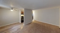 This single-floor unit offers a straightforward, functional layout with clearly defined living zones. The open living area features a combination of wood-look hard flooring and plush carpeting, neutral gray walls, and a textured ceiling. A wall-unit air conditioner and baseboard heating provide year-round climate control, while vertical blinds on the windows manage natural light effectively.

The kitchen is accessible directly from the living area and is equipped with warm-toned wood cabinetry featuring raised-panel doors, light granite-look countertops, a stainless steel sink, and black appliances including a refrigerator, dishwasher, and range. The wood-look flooring continues throughout the kitchen, adding visual continuity.

The bedroom is a well-proportioned, carpeted room with neutral beige walls, a textured ceiling, and a window fitted with vertical blinds that allows for ample natural light. The room offers a calm, understated atmosphere.

The bathroom is finished in a clean, all-white palette with a combined bathtub and shower, a toilet, and a vanity with a sink. A lighted mirror above the vanity provides practical illumination, and a window above the tub brings in natural light while maintaining privacy.