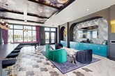 This striking single-floor amenity space makes an immediate impression through its bold, eclectic interior design and exceptional urban views. A wide entry corridor welcomes visitors with marble-and-dark-tile flooring, floor-to-ceiling windows overlooking the cityscape, and a curated gallery wall of framed artwork, setting an artistic tone from the outset.

The main gathering area is expansive and open, anchored by a stunning coffered ceiling adorned with large-scale floral and figurative murals, adding a dramatic artistic focal point overhead. The flooring transitions between large-format white marble tiles and a geometric hexagonal tile pattern, delineating distinct zones within the space. A richly decorated lounge area features plush emerald velvet and charcoal upholstered seating arranged around an organic-shaped marble coffee table, complemented by deep plum drapery framing the floor-to-ceiling windows.

A teal cabinetry wet bar with a textured mosaic backsplash serves as a functional centerpiece, while a billiards table offers additional entertainment. The space opens directly onto a furnished outdoor terrace, providing sweeping skyline views and an ideal setting for gatherings. Throughout, the design balances vibrant color, luxurious materials, and abundant natural light.