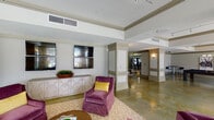 Located at 145 Amberleigh Drive in Wilmington, NC, this single-floor community amenity facility offers a well-appointed collection of gathering and recreational spaces designed for comfort and functionality. Throughout the interior, polished concrete floors, elevated ceilings with crown molding, and panel-detailed columns establish a refined yet approachable architectural character. Track lighting complements the abundant natural light that pours in through large banks of windows, offering views of the surrounding landscaped grounds.

The main lounge area serves as the centerpiece of the space, furnished with plush burgundy armchairs, a neutral sofa, and a patterned area rug, all arranged to encourage conversation and relaxation. Dual flat-screen televisions mounted above a geometric-patterned credenza add a media-ready element to this seating zone. A secondary lounge alcove provides a more intimate setting with a sectional sofa and abstract wall art. The kitchen area features granite countertops, ample cabinetry, a large sink, and a standout iridescent mosaic tile accent wall framing a wall-mounted television. A billiards room and a glass-enclosed fitness center with visible exercise equipment round out the amenities, making this a versatile and well-equipped communal facility.