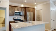 This single-floor residence offers a thoughtfully designed layout that balances comfort and functionality. The open-concept kitchen and living area serves as the heart of the home, showcasing rich dark-stained wood cabinetry, a classic white subway tile backsplash, and a generously sized granite island with an undermount sink and pendant lighting overhead. Stainless steel appliances, including a French door refrigerator, electric range, and built-in microwave, complete the kitchen's modern aesthetic. Light wood-look flooring flows through the main living area, enhancing the bright and airy atmosphere created by natural light from the entryway windows. The bedrooms are finished with plush wall-to-wall carpet and neutral tones, providing a calm retreat. A spacious walk-in closet with wire shelving offers ample storage. The primary bathroom features large-format tile flooring, a dual-sink vanity with wood cabinetry and granite countertops, and a glass-enclosed walk-in shower with full tile surround. A secondary bathroom includes a soaking tub with a matching tiled surround. A dedicated laundry area accommodates a full-size washer and dryer side by side, adding everyday convenience to this well-equipped residence.