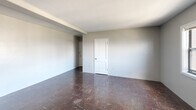 Located at 1230 Pendleton Street in Columbia, SC, this single-floor unit offers three bedrooms and one bathroom within a compact, efficiently organized layout. The space features dark parquet-style flooring throughout, lending a consistent look across the common areas and bedrooms. Neutral gray and white walls keep the interior feeling open and uniform.

The spacious primary bedroom is notably generous in size, offering ample room for furnishings. The two additional bedrooms are more modest in scale, each featuring windows with blinds that allow for natural light and window-unit air conditioning. One bedroom is distinguished by vertical board paneling along its walls, adding a subtle textural detail.

The bathroom is fitted with classic white square tile surrounding a full tub-shower combination, complemented by a wall-mounted mirror and a pedestal sink — a clean, functional design. A dedicated laundry room includes a double utility sink, white cabinetry with open shelving above, a window overlooking the surrounding cityscape, and space for appliances. Two hallways connect the rooms, providing a logical flow throughout the unit. Overall, this unit presents a straightforward, utilitarian layout well-suited for practical urban living in downtown Columbia.