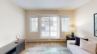 Located in the Ellerslie neighbourhood of southwest Edmonton, this 2-bedroom, 2-bathroom residence offers a thoughtfully designed single-level layout with a functional and welcoming flow throughout. The open-concept living, dining, and kitchen area forms the heart of the home, with warm hardwood-style flooring, a textured ceiling, and natural light streaming in through large windows and a sliding patio door that opens to a private balcony. The kitchen is well-equipped, featuring rich warm-toned cabinetry, granite-style countertops, a mosaic tile backsplash, and full-size black appliances including a refrigerator, electric range, and built-in microwave. The adjoining dining area is illuminated by a pendant light fixture, creating an inviting space for everyday meals. The primary bedroom is a comfortable retreat with a closet, hardwood-style flooring, and a window with outdoor views. The second bedroom is similarly sized and well-lit. Both bathrooms are finished with tile flooring, warm wood vanities, and granite-style countertops; one features a stand-up glass shower. Four closets and an in-unit laundry room provide excellent storage and convenience throughout the home.