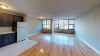 This one-bedroom, one-bathroom unit at 1 Woodbine Ave in Avenel, NJ offers a well-designed single-floor layout with a clean, modern aesthetic throughout. Warm hardwood flooring flows seamlessly across the living area, bedroom, and hallway, lending a cohesive and inviting feel to the space. The expansive living area is bathed in natural light through a wide bank of large windows fitted with blinds, complemented by baseboard heating along the perimeter walls. The kitchen is a standout feature, boasting rich dark cabinetry with ample storage, stainless steel appliances including a gas range, microwave, and refrigerator, a marble-style tile backsplash, and light tile flooring — offering both style and functionality. The bedroom is generously sized, offering a double closet with white panel doors and its own window that fills the room with natural light. Additional wall space provides versatile layout options. The bathroom is finished with full-height white tile surrounding a soaking tub and shower combination, brushed nickel fixtures, and a clean white vanity. Throughout the unit, soft gray walls create a calm, neutral backdrop that complements the warm wood floors and modern finishes, making this a practical and comfortable living space.