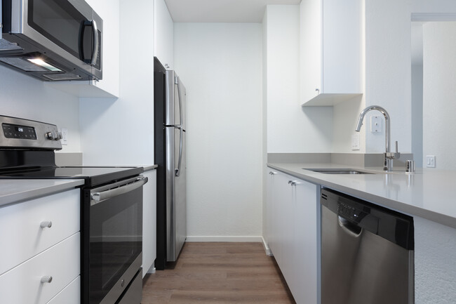 Renovated Package I kitchen with stainless steel appliances, grey quartz countertops, white cabinetry, and hard surface flooring - eaves West Valley