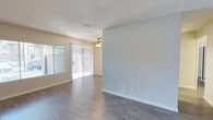 This single-floor space offers a clean, functional layout with a welcoming sense of openness. The main living area is finished with smooth, gray-toned laminate flooring that adds a contemporary feel underfoot, complemented by crisp white baseboards that frame each room with a polished touch. Neutral light gray walls provide a versatile backdrop, making the space feel airy and easy to personalize.

A ceiling fan with an integrated light fixture is centrally positioned, ensuring comfortable airflow throughout. The living area is bathed in natural light, courtesy of a sliding glass door fitted with vertical blinds, which also provides convenient access to the outdoors. An additional window further enhances the brightness of the space, maintaining a light and pleasant ambiance throughout the day.

The textured popcorn ceiling adds a classic residential character, while the HVAC vent is neatly integrated into the ceiling for efficient climate control. The overall design is straightforward and practical, offering a move-in-ready environment with a neutral palette that easily accommodates a variety of interior styles. The combination of natural light, modern flooring, and clean finishes makes this a comfortable and inviting single-story space.