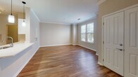 Located at 1000 Presidents Way in Dedham, Massachusetts, this single-floor residence offers a thoughtfully designed layout with consistent hardwood-style flooring throughout. The living area is bright and welcoming, featuring elegant crown molding, neutral warm-toned walls, and generous natural light streaming through large windows fitted with blinds. A track light fixture adds a modern touch to the space, while clean white panel doors and crisp baseboards lend a polished, cohesive aesthetic.

The galley-style kitchen is well-equipped with stainless steel appliances, including a range, built-in microwave, refrigerator, and dishwasher. White shaker cabinetry pairs with light quartz countertops and a subtle tile backsplash, creating a clean and functional cooking environment. The kitchen opens toward a hallway, providing easy flow throughout the unit.

A secondary room with dual windows offers abundant natural light and views of the surrounding area, making it a versatile space suitable as a bedroom or home office. The walk-in closet features wire shelving on multiple walls, providing generous storage capacity.

The bathroom is neatly finished with a white vanity, quartz countertop, a framed mirror, white overhead cabinetry, and a tub-shower combination with tiled surround. Hardwood-style flooring extends into the bathroom, tying together the uniform design found throughout this well-maintained residence.