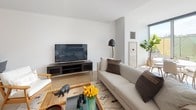 This contemporary multi-floor residence showcases a thoughtfully designed open-concept layout with clean lines and modern finishes. The living area is bright and welcoming, featuring light hardwood flooring, large windows that invite natural light, and access to an outdoor space. The kitchen is a standout, equipped with stainless steel appliances, white and gray cabinetry extending to the ceiling, a large island with a gray quartz countertop, pendant lighting, and bar-height seating — ideal for casual dining and entertaining. The living room offers generous space for comfortable seating arrangements, complemented by a TV media console and views toward the outdoors. The residence includes multiple bedrooms, each with light hardwood floors, ample closet storage, and large windows. The primary bedroom features an en-suite bathroom with a double vanity, floating gray cabinetry, a glass-enclosed shower, and tiled flooring. A second bathroom maintains the same refined aesthetic with a floating vanity and neutral tile floors. A dedicated office or flex space adds further versatility to the layout. Spread across three floors, this residence offers a well-organized and functional flow, combining modern architecture with a warm, livable ambiance throughout.
