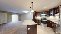 Located at 1021 Hope St in Mankato, MN, this 2-bedroom, 1-bathroom unit offers a well-designed single-floor layout with a thoughtful mix of functionality and comfort. The open-concept kitchen and living area serves as the heart of the home, where rich dark-wood cabinetry with raised-panel detailing pairs with granite countertops and a center island perfect for casual dining or meal prep. A full suite of stainless steel appliances — including a French door refrigerator, range, microwave, and dishwasher — adds a polished, modern touch, while tile flooring grounds the kitchen space. The living room extends naturally from the kitchen, featuring plush carpeting, neutral warm-toned walls, and a large sliding glass door that fills the room with natural light and provides access to a private balcony. Both bedrooms are generously proportioned, with soft carpeting, ceiling fans, and ample closet space — including three closets throughout the unit. The bathroom features a full tub/shower combination with brushed nickel fixtures and tile flooring. A dedicated in-unit laundry room with side-by-side washer and dryer adds everyday convenience, while a separate utility room rounds out the practical layout of this well-appointed home.