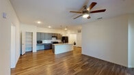 This ADA-compliant, single-story, three-bedroom, two-bathroom unit in Zachary, Louisiana is thoughtfully designed to balance accessibility with modern style. The open-concept living and kitchen area forms the heart of the home, anchored by a granite-topped center island with a double sink and stylish pendant lighting overhead. The kitchen is well-appointed with gray cabinetry, light granite countertops, a tile backsplash, and black appliances including a range, microwave, and refrigerator. Wood-style plank flooring runs throughout the main living areas, and a ceiling fan enhances comfort in the spacious living room, which receives natural light through a glass-panel exterior door. An in-unit washer is conveniently located just off the kitchen.

The bedrooms feature plush carpeting, ceiling fans, and windows that bring in ample natural light. The two bathrooms reflect consistent design choices: one features an ADA-compliant open vanity with granite countertop and wood-style flooring, while the second includes a tub-shower combination. The layout, visible in the floor plan, offers a logical flow between living, sleeping, and utility spaces, making this unit both functional and comfortable.