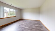 Located at 825 Talcott Ave in Lemont, IL, this single-floor, one-bedroom, one-bathroom unit offers a practical and well-organized layout across a compact but efficiently designed footprint. The combined kitchen and living area serves as the heart of the unit, where the kitchen features warm oak cabinetry, white laminate countertops, white appliances including a range and refrigerator, and durable wood-look vinyl plank flooring. A large multi-pane window in the kitchen/living area allows generous natural light and provides views of the surrounding greenery. The living room area continues the vinyl plank flooring and offers a clean, neutral palette with warm wood baseboards throughout. The bedroom is a comfortable, well-proportioned room finished with plush wall-to-wall carpeting, soft green accent walls, and two bi-fold wood panel closets offering ample storage. A large window brings in natural light and outdoor views. The bathroom is finished with wood-look vinyl flooring, an oak vanity with a white countertop, a large mirror, and accessibility grab bars. A dedicated utility room houses the mechanical systems. Overall, the unit presents a clean, functional, and move-in ready atmosphere with consistent warm wood tones throughout.