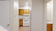 This two-story home offers a practical and well-organized layout across two floors. The main level, which comprises the larger share of the total floor area, features a combined kitchen and living room, a dedicated laundry area, and a bathroom. The kitchen is equipped with warm wood-toned cabinetry, a white electric range, a refrigerator, and tile flooring, with a pass-through counter that connects to the living area. The living room is bright and inviting, featuring warm hardwood-style flooring, a sliding glass door that opens to an outdoor view, and an additional window that allows natural light to fill the space. The upper level houses both bedrooms and two additional bathrooms. The primary bedroom is a comfortably sized retreat with soft carpet flooring, a ceiling fan, and direct access to an en-suite bathroom with vanity cabinetry. The second bedroom also features hardwood-style flooring and ample space. The three bathrooms throughout the home include tub-shower combinations and vanity storage. Textured ceilings are consistent throughout the home, adding a classic touch to the overall aesthetic. Two staircases connect the floors, providing convenient circulation within the home.