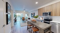 Located at 632 SW 150th St in Burien, WA, this thoughtfully designed unit offers a seamless open-concept layout where the kitchen, dining, and living areas flow naturally into one another. The kitchen is outfitted with stainless steel appliances, including a refrigerator, electric range, microwave, and dishwasher, complemented by warm wood-toned upper cabinetry, gray lower cabinets, and clean white countertops. A freestanding dining table with bar-height seating serves as a natural transition between the kitchen and the living space. The living area is bright and airy, featuring a ceiling fan, light wood-style flooring, and large sliding glass doors that open onto a private balcony with outdoor views of the surrounding greenery. The bedroom is a calm retreat with a sliding closet, a window that brings in natural light, and wood-style flooring that carries throughout the unit. The bathroom features a sleek, modern vanity with a white quartz countertop, undermount sink, and a large mirror, maintaining the clean aesthetic found throughout the home. Recessed lighting and a neutral white palette tie each space together, creating a cohesive and contemporary living environment.