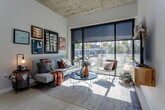 Located at 211 W Armour Blvd in Kansas City's vibrant Midtown neighborhood, this single-floor unit showcases an industrial-modern aesthetic with notable architectural character. The living area is a standout, featuring soaring exposed concrete ceilings and expansive floor-to-ceiling windows fitted with solar shades, flooding the space with natural light while offering views of the surrounding neighborhood. A floating wood media console and coordinating wall shelf add a warm, contemporary touch to the main living space.

The kitchen is thoughtfully designed with light wood cabinetry, sleek dark countertops, a white subway tile backsplash, and stainless steel appliances, including a built-in microwave and dishwasher. Open shelving provides additional display and storage options. A dedicated dining area sits adjacent to the kitchen, completing the functional open-plan layout.

The bathroom features a wood-toned vanity with a quartz countertop, undermount sink, and dark tile wainscoting, delivering a clean, modern finish. A combined laundry area includes a stacked washer and dryer unit alongside organized closet rod storage, offering excellent in-unit convenience. Throughout the space, the consistent use of neutral tones, natural materials, and industrial accents creates a cohesive and contemporary living environment.
