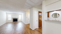 This single-story, 2-bedroom, 2-bathroom residence offers a thoughtfully designed layout that balances comfort and functionality. The open-concept living and dining area is highlighted by warm hardwood-style flooring, a textured ceiling, and a classic wood-burning fireplace flanked by two windows that allow natural light to fill the space. Structural columns add architectural character while subtly defining the flow between areas.

The kitchen features warm wood cabinetry, a granite-style countertop with a pass-through window to the living area, a black dishwasher and refrigerator, and a sink positioned beneath a decorative round mirror — combining practicality with a clean aesthetic.

A dedicated hallway leads to the private quarters, where both bedrooms are outfitted with plush wall-to-wall carpeting and ceiling fans with integrated lighting. The primary bedroom is generously sized, while a secondary bedroom opens directly to an outdoor balcony through sliding glass doors, offering pleasant exterior views.

Each bathroom includes a full tub-and-shower combination elegantly finished with large-format, marble-style wall tiles in warm neutral tones and hardwood-style flooring. The unit also includes two closets and a dedicated entrance, providing ample storage and a welcoming arrival experience.