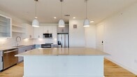 This thoughtfully designed single-floor residence offers three bedrooms, two bathrooms, four closets, and a dedicated laundry room, delivering a well-rounded and functional layout. The open-concept kitchen and living area serves as the heart of the home, anchored by a large central island with a sleek quartz countertop and pendant lighting above. The kitchen features two-tone cabinetry — crisp white upper cabinets paired with soft blue-gray lower cabinets — complemented by a white tile backsplash, stainless steel appliances, and generous open shelving. Light hardwood flooring flows seamlessly throughout the entire space, enhancing the bright, airy atmosphere. The living area benefits from natural light through multiple windows and sliding glass doors, with a ceiling fan adding comfort. Each bedroom is well-proportioned, with large windows and ceiling fans. The primary bedroom connects to a spacious walk-in closet with built-in shelving and hanging rods. The bathrooms are finished with neutral large-format tile flooring, tub-shower combinations with tiled surrounds, and white vanities with dark hardware accents. The in-unit laundry room accommodates a full-size washer and dryer with overhead shelving for added storage.
