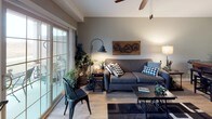 This thoughtfully designed single-floor residence showcases a cohesive industrial-rustic aesthetic throughout its well-connected living spaces. The kitchen stands out with rich, dark cabinetry, granite countertops, stainless steel appliances including a gas range and built-in microwave, and light hardwood-style flooring — offering both functionality and visual appeal. A bright, open-concept living area flows naturally from the kitchen, featuring large sliding glass doors that flood the space with natural light and provide direct access to an outdoor patio with open views. The living room is accented by a ceiling fan, light wood flooring, and distinctive industrial wall décor. A cozy flex room with carpeted floors, elevated shelving, and ample natural light serves well as a home office or sitting room. The bedroom offers a tranquil retreat with plush carpet, a ceiling fan, wrought iron bed frame, and windows that bring in warm, diffused light. The bathroom is finished with granite countertops, dark cabinetry consistent with the kitchen, a glass-enclosed shower, and wood-look tile flooring. A wide, light-filled entry hallway connects the spaces seamlessly, enhancing the overall sense of flow and openness throughout this well-curated home.
