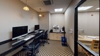 Located at 2500 Clarendon Blvd in Arlington, Virginia, this single-floor business center is designed to meet the productivity needs of guests and visitors. The room features a sleek, built-in desk running along the walls, accommodating multiple iMac computer workstations equipped with keyboards and mice, providing ample space for simultaneous users. Ergonomic mesh-back chairs are positioned at each station, ensuring comfort during extended work sessions. Pendant lighting fixtures hang from the drop-panel ceiling, supplemented by recessed fluorescent lighting to create a well-lit workspace. A dedicated area along one wall houses a multifunction printer and copier atop a storage cabinet, accompanied by a recycling bin, ensuring all essential office needs are met in one place. The floor is covered in a patterned carpet with a geometric motif, adding a touch of visual interest to the otherwise neutral, professionally toned interior. A glass-paneled door with a black frame connects the business center to the broader lobby area, offering a view of the bright, open lounge beyond. The space is compact yet efficiently arranged, making it a convenient and fully equipped stop for travelers requiring reliable workspace access.