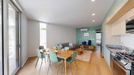 Located in the desirable West Los Angeles neighborhood of 1503–1507 S Barrington Ave, this modern 5-bedroom, 4-bathroom residence offers a thoughtfully designed single-floor layout with clean, contemporary finishes throughout. The open-concept kitchen and living room serves as the heart of the home, featuring light hardwood flooring, recessed lighting, and large sliding glass doors that connect seamlessly to an outdoor balcony, flooding the space with abundant natural light. A teal accent wall adds a pop of color to the living area, complementing the neutral white walls and warm wood tones found throughout. Each of the five bedrooms maintains a minimalist aesthetic with crisp white walls, light wood flooring, and individual wall-mounted air conditioning units for personalized climate control. The bedrooms are well-lit by large windows that frame views of the surrounding West LA cityscape. Each bedroom is paired with a dedicated closet for ample storage. The four bathrooms are sleekly finished in white tile, featuring wall-mounted vanities with light wood cabinetry, modern fixtures, and walk-in shower stalls with clean subway tile surrounds. Sage green flooring in the bathrooms provides a subtle, contemporary contrast to the otherwise bright interiors. A dedicated laundry room and multiple hallways complete the efficient, well-organized floor plan of this modern Los Angeles residence.