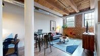 Located at 150 Oakland St in Mansfield, MA, this single-floor loft unit masterfully blends industrial character with modern comfort. The open living area immediately impresses with its soaring wood beam ceilings, exposed ductwork, and original brick accent walls that speak to the building's rich architectural heritage. Light wood flooring runs throughout, complementing the warm tones of the reclaimed timber above. Large industrial-style windows flood the space with natural light, further enhancing the airy, open feel.

The kitchen is well-appointed with rich, dark cabinetry, granite countertops, a classic subway tile backsplash, and a full suite of stainless steel appliances, including a gas range, microwave, refrigerator, and dishwasher. A dedicated office area provides a quiet, functional workspace with soaring ceilings and ample room for productivity.

The bedroom features dramatic exposed wood beams overhead, a spacious closet, and direct access to a well-designed bathroom finished with granite countertops and neutral tile flooring. A dedicated in-unit laundry room with a stacked washer and dryer adds everyday convenience. Throughout the space, the thoughtful balance of historic architectural elements and contemporary finishes creates a distinctive and inviting atmosphere.