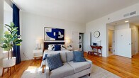 Located at 1198 Main St in Bridgeport, Connecticut, this thoughtfully designed studio offers a seamless blend of modern aesthetics and practical functionality across a single-floor layout. Warm hardwood flooring extends throughout the main living area, creating a cohesive and inviting atmosphere brightened by large windows dressed with navy curtains that allow generous natural light to fill the space.

The open main area is versatile, comfortably accommodating a sleeping area, a seating zone, and a dedicated workspace with a mid-century style desk. A compact dining nook adds further functionality, while bold, contemporary artwork lends the space a curated, modern character.

The kitchen is well-equipped with stainless steel appliances, including a full-size refrigerator, range, and microwave. Cabinetry features a two-tone design with white upper cabinets and warm wood-toned lower cabinets, complemented by a classic white subway tile backsplash.

The bathroom is clean and modern, featuring a soaking tub with a subway-tiled surround, a warm wood vanity with a white countertop, and a mirrored medicine cabinet. Notably, the unit includes an in-unit stacked washer and dryer tucked neatly within a dedicated closet. This unit offers an efficient, stylish living experience in the heart of Bridgeport.