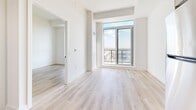 Located at 2475 Old Bronte in Oakville, Ontario, this well-designed one-bedroom, one-bathroom unit offers a thoughtfully organized layout across a single floor. Light oak-toned hardwood flooring runs throughout the space, complementing the clean white walls and creating a bright, cohesive aesthetic.

The entrance opens into a hallway flanked by a sliding-door closet, providing immediate storage upon arrival. The open-concept living area flows directly into the kitchen, which features light wood cabinetry, stainless steel appliances including a refrigerator, oven, and built-in microwave, and a streamlined countertop with an integrated sink.

The living room benefits from an abundance of natural light and provides access to a private balcony through a large floor-to-ceiling window, offering elevated views of the surrounding Oakville neighbourhood. The bedroom is a comfortable, well-proportioned space with its own sliding double-door closet and direct balcony access, further enhancing the sense of openness.

The bathroom is finished in a modern style with a glass-enclosed walk-in shower featuring black hardware accents, wood-toned vanity cabinetry, and consistent light flooring. In-unit laundry is also included, adding everyday convenience. Overall, the unit presents a clean, contemporary living environment with practical amenities throughout.