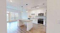 This single-floor residence offers a clean, contemporary design highlighted by a cohesive palette of crisp whites and warm natural tones throughout. The kitchen serves as the centerpiece of the open-concept living area, showcasing tall white shaker cabinetry, a decorative scalloped tile backsplash, and granite countertops. A substantial center island with built-in open shelving and matching granite surface provides additional prep and storage space, illuminated by two stylish pendant lights. Stainless steel appliances, including a range, microwave, dishwasher, and refrigerator, complete the well-appointed kitchen. Track lighting adds further brightness, complementing the natural light that pours in through large windows fitted with horizontal blinds.

Light wood-tone laminate flooring runs throughout the main living and kitchen areas, creating a warm, unified feel. The bedrooms are finished with plush neutral carpeting and generous windows that invite ample natural light. The bathroom features wood-look luxury vinyl flooring, a granite-topped vanity with white cabinetry, and a soaking tub enclosed by elegantly tiled marble-look surround with an arched glass partition. The overall ambiance is bright, airy, and move-in ready.