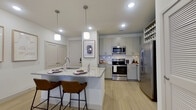 This single-floor residence showcases a thoughtfully designed open-concept layout with light hardwood-style flooring running throughout. The kitchen serves as the heart of the home, anchored by a granite-topped island with an undermount sink and seating for two. Gray shaker-style cabinetry lines the walls, complemented by a decorative arabesque tile backsplash, stainless steel appliances including a range, over-the-range microwave, refrigerator, and dishwasher, plus a built-in wine rack for added functionality.

The kitchen flows seamlessly into the living area, which benefits from natural light through a set of double doors framed by wide blinds. A ceiling fan overhead and neutral walls contribute to a calm, airy atmosphere.

The bedroom is a comfortable retreat featuring a ceiling fan, a generous window with drapery, and direct access to a walk-in closet outfitted with wire shelving and hanging rods. The adjoining bathroom offers a granite-topped vanity with sage-toned cabinetry, a shower with curtain enclosure, and clean, bright finishes throughout. Recessed lighting and pendant fixtures maintain a cohesive modern aesthetic across the entire space.