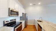 This single-story unit in Southaven, Mississippi, offers a thoughtfully designed layout with consistent hardwood-style flooring and neutral gray tones that create a clean, cohesive aesthetic throughout. Crown molding adds a refined architectural detail visible across the main living and kitchen areas.

The kitchen is well-equipped with stainless steel appliances, including an electric range, over-the-range microwave, refrigerator, and dishwasher. White shaker-style cabinetry with brushed nickel hardware pairs with light granite countertops to create a bright, functional workspace. A peninsula counter with overhang connects the kitchen to the open living area, which provides generous space for a variety of furniture arrangements.

The bedroom features a ceiling fan, a window with natural light, and ample wall space. An adjoining hallway leads to the bathroom, which includes a tiled walk-in shower, and connects to a dedicated walk-in closet with built-in shelving rods.

Additional highlights include an in-unit laundry area with a full-size washer and dryer, built-in open shelving near the kitchen, and recessed lighting throughout. The overall design prioritizes functionality and a clean, modern aesthetic.