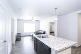 This single-floor unit offers a practical and modern layout designed for comfortable everyday living. The kitchen is a standout feature, equipped with dark espresso cabinetry, granite-style countertops, and a full suite of black appliances including an electric range, microwave, dishwasher, and refrigerator. Light wood-style flooring runs throughout the main living areas, lending a clean and cohesive look. The kitchen flows naturally toward the living area, which is bright and inviting, featuring a ceiling fan, a large window that draws in natural light, and light-toned walls that create an airy atmosphere. Two bedrooms provide comfortable private spaces, each carpeted and furnished with a bed frame, desk, and storage. One bedroom also includes a dedicated closet. The unit features two bathrooms, each appointed with dark vanity cabinetry, stone-look countertops, and wood-style flooring, maintaining a consistent design aesthetic throughout. A dedicated laundry area near the entry houses a full-sized washer and dryer, adding significant everyday convenience. The entryway is clean and functional, with neutral walls and durable flooring. Overall, the unit presents a cohesive, modern interior well-suited for practical, comfortable living.