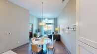 Located at 1212 S Rangeline Rd in Carmel, Indiana, this single-floor residence offers a thoughtfully designed open-concept layout with modern finishes and a bright, welcoming ambiance. The living and dining areas flow seamlessly together, anchored by stylish pendant lighting and a starburst chandelier that add a contemporary flair. Large windows and sliding glass doors flood the space with natural light while offering pleasant outdoor views, creating an airy and spacious feel throughout. The kitchen is a functional centerpiece, featuring granite countertops, a two-seat island with pendant lighting overhead, stainless steel appliances, and crisp white cabinetry contrasted by slate-blue lower cabinets. Wood-look flooring runs consistently throughout, tying all areas together cohesively. The bedroom is a serene retreat with generous window coverage, allowing soft natural light to filter in. The bathroom is well-appointed with a wide vanity, ample counter space, and tall ceilings that contribute to an open feel. A hallway with closet access connects the private quarters to the main living space, ensuring a practical and efficient floor plan. The overall aesthetic is clean, contemporary, and inviting, with neutral tones and modern accents throughout.