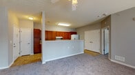 This single-floor residence offers a clean, functional layout designed for comfortable everyday living. The open-concept living area is anchored by soft, wall-to-wall carpeting and a ceiling fan overhead, creating a relaxed and airy atmosphere. Large windows and a glass-panel exterior door flood the space with natural light while offering views of the surrounding greenery outside.

The galley-style kitchen is a standout feature, lined on both sides with warm-toned wooden cabinetry that provides generous storage. Light-colored countertops run the length of the kitchen, complementing the white appliances, which include a coil-top electric range, refrigerator, and dishwasher. Tile flooring and overhead fluorescent lighting keep the kitchen bright and easy to maintain. A half-wall peninsula separates the kitchen from the living area, offering a natural transition between spaces.

The bedroom is a quiet, well-proportioned room featuring the same plush carpeting found throughout the living areas, a ceiling fan, and a window that invites natural light. The bathroom is thoughtfully designed with accessibility in mind, featuring multiple stainless steel grab bars positioned near the bathtub and toilet, along with durable tile flooring. Neutral gray walls throughout the residence lend the space a cohesive, modern feel.