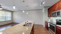 Located at Barrett Lakes Blvd NW in Kennesaw, Georgia, this single-story, one-bedroom, one-bathroom residence offers a thoughtfully designed open-concept layout. The combined kitchen and living area serves as the heart of the home, featuring rich dark-wood cabinetry, granite countertops, a large kitchen island with a double stainless steel sink, pendant lighting, and a full suite of stainless steel appliances including a refrigerator, range, and microwave. Track lighting and hardwood-style flooring add a polished, modern touch to the kitchen and living spaces. The living room is bright and airy, with multiple windows allowing generous natural light and views of lush greenery. A ceiling fan overhead enhances comfort throughout the space. The bedroom is a comfortable retreat with plush carpet flooring, a ceiling fan, and a wide window framing verdant outdoor views. A dedicated closet provides practical storage. The bathroom is finished with tile flooring, a granite-topped vanity with rich wood cabinetry, a framed mirror, and a tub-shower combination. A hallway connects the living areas to the private spaces, completing the efficient and functional floor plan of this well-designed Kennesaw residence.