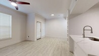 This thoughtfully laid-out 1-bedroom, 1-bathroom residence spans a single floor and offers a clean, modern aesthetic throughout. The open living area greets you with light-toned wood-look flooring, crisp white walls, and built-in shelving that adds both function and character. A ceiling fan with a striking red accent and multiple windows with white blinds fill the space with natural light, creating a bright and airy atmosphere. A private entrance door with a sidelight window adds convenience and accessibility.

The kitchen is well-appointed with taupe shaker-style cabinetry featuring black hardware, stainless steel appliances including a slide-in range and dishwasher, and a marble-look tile backsplash that lends an upscale touch. Light wood-look flooring continues seamlessly from the living area into the kitchen.

The bedroom is carpeted and comfortably sized, featuring a ceiling fan and a window that invites natural light. It offers direct access to a dedicated walk-in closet with built-in shelving and hanging rods, providing generous storage. The full bathroom is finished with neutral floor tile, white subway tile surrounding the soaking tub, and cabinetry above the toilet for additional storage. A hallway connects the private areas of the home, completing the efficient and functional floor plan.