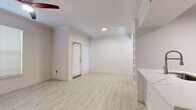 This thoughtfully laid-out 1-bedroom, 1-bathroom residence spans a single floor and offers a clean, modern aesthetic throughout. The open living area greets you with light-toned wood-look flooring, crisp white walls, and built-in shelving that adds both function and character. A ceiling fan with a striking red accent and multiple windows with white blinds fill the space with natural light, creating a bright and airy atmosphere. A private entrance door with a sidelight window adds convenience and accessibility.

The kitchen is well-appointed with taupe shaker-style cabinetry featuring black hardware, stainless steel appliances including a slide-in range and dishwasher, and a marble-look tile backsplash that lends an upscale touch. Light wood-look flooring continues seamlessly from the living area into the kitchen.

The bedroom is carpeted and comfortably sized, featuring a ceiling fan and a window that invites natural light. It offers direct access to a dedicated walk-in closet with built-in shelving and hanging rods, providing generous storage. The full bathroom is finished with neutral floor tile, white subway tile surrounding the soaking tub, and cabinetry above the toilet for additional storage. A hallway connects the private areas of the home, completing the efficient and functional floor plan.