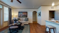 This single-floor residence is thoughtfully designed with a cohesive blend of comfort and functionality. The living area serves as the heart of the home, featuring rich hardwood-style flooring, crown molding, and a ceiling fan overhead. Large windows dressed with floor-length drapes allow generous natural light to fill the space, while a set of French doors provides additional brightness and outdoor access. An elegant arched passageway connects the living area to the rest of the unit, adding a refined architectural detail.

The kitchen is a standout feature, equipped with dark espresso cabinetry, granite countertops, stainless steel appliances, and a peninsula with bar seating illuminated by pendant lighting — ideal for casual dining and entertaining.

The primary bedroom is carpeted for comfort and includes a ceiling fan, a large window with decorative drapes, and ample room for furnishings. The secondary bedroom also features plush carpeting and convenient access to a well-organized walk-in closet with built-in shelving.

The bathroom is finished with matching dark cabinetry, granite countertops, a large vanity mirror, and a full tub-shower combination with tile surround. A dedicated in-unit laundry area with a full-size washer and dryer adds everyday convenience to this well-rounded residence.