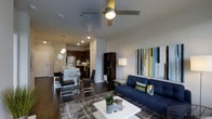 This well-designed 1-bedroom, 1-bathroom unit offers a thoughtfully organized open-concept floor plan that maximizes every square foot. The living area is anchored by rich dark hardwood flooring, a ceiling fan with integrated lighting, and recessed ceiling lights that create a warm, inviting ambiance. A bold navy sofa, geometric area rug, and vibrant abstract wall art lend the space a modern, curated aesthetic.

The living and dining areas flow seamlessly together, with a compact dining set positioned near a breakfast bar that connects directly to the kitchen. The kitchen is equipped with stainless steel appliances, including a full-size refrigerator, dark cabinetry, and pendant lighting that adds a stylish focal point above the counter.

A freestanding shelving unit serves as a subtle divider between the living and kitchen zones, adding both function and visual interest. The open layout ensures a natural flow throughout the main living space, making it feel spacious and connected.

The unit's contemporary design, cohesive color palette of navy, yellow, and grey, and quality finishes throughout create a polished, move-in-ready environment ideal for those seeking a modern and functional living experience.